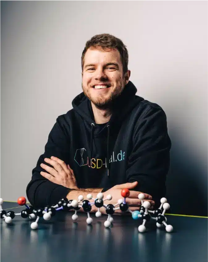 A man in a hoodie with lsd legal label sitting in front of a table full of molecule models.